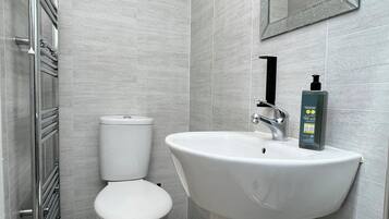 A modern bathroom with a white toilet, a pedestal sink, and a mirror above the sink.