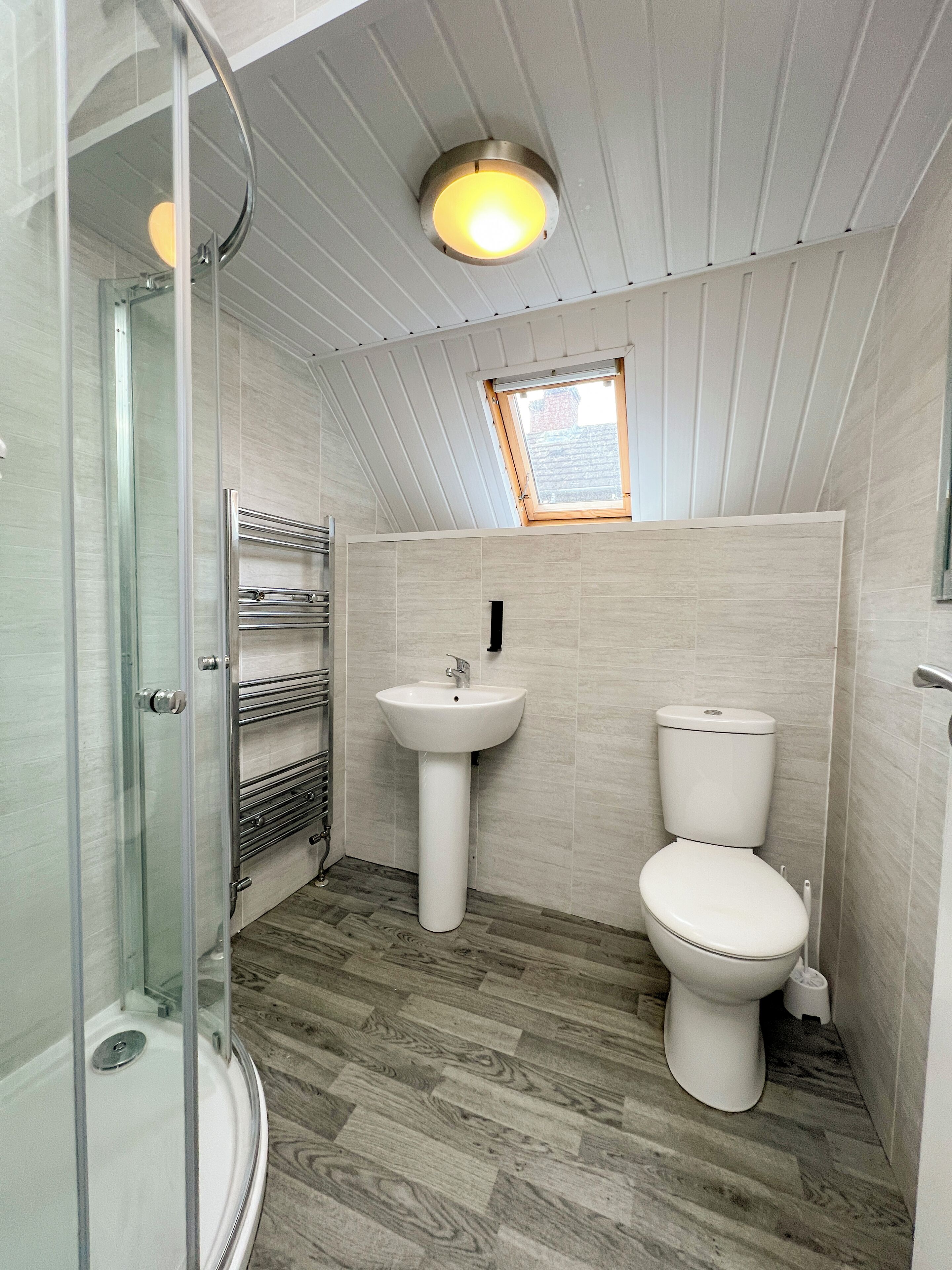 Ein Badezimmer mit Dusche, Waschbecken und Toilette, mit schrägverdeckter Decke und Holzboden.