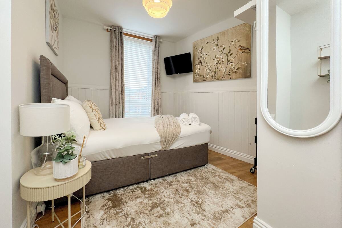 A bedroom with a bed, bedside table, lamp, and a large mirror.