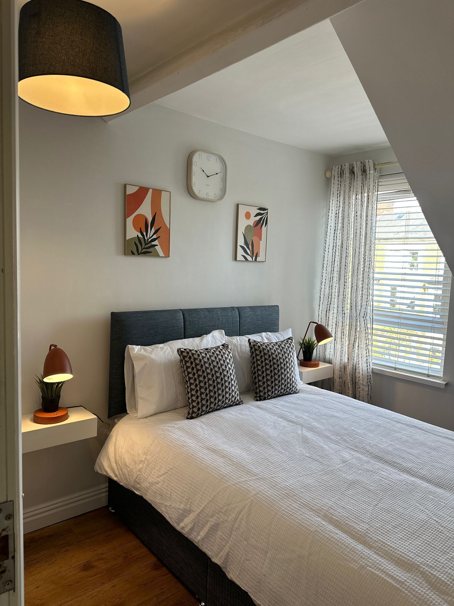A modern bedroom with a large bed, a wall clock, and abstract art.