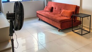 A modern living room with a red sofa, a standing fan, and a window with a view of a building. - Flat Studio Everest: Your Accommodation in Boa Viagem (Recife)
