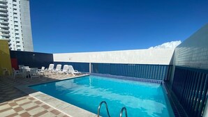 A swimming pool with a tiled deck and lounge chairs. - Flat Studio Everest: Your Accommodation in Boa Viagem (Recife)
