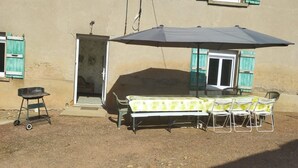 An outdoor patio with a table and chairs, a grill, and a covered area.