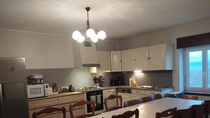 A modern kitchen with white cabinets, a dining table with chairs, and a view of the outdoors through a window.