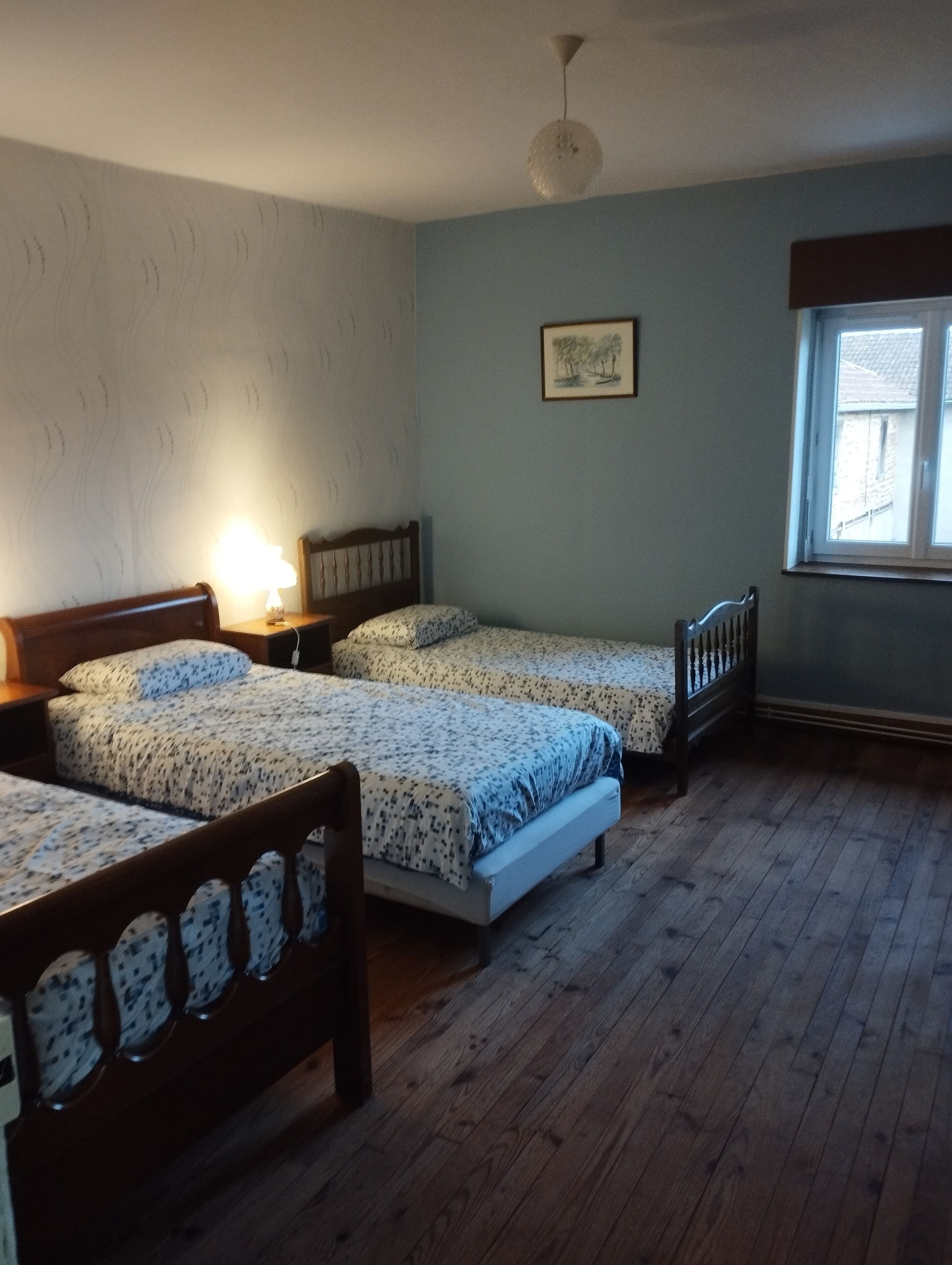 A room with two wooden beds, a wooden headboard, a single window, and a wall-mounted picture.
