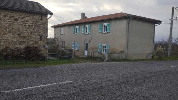 A two-story building with a stone wall on the left, a red-tiled roof, and a gravel driveway.