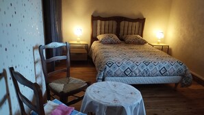 A bedroom with a bed, two bedside tables with lamps, a chair, and a small table with a tablecloth.