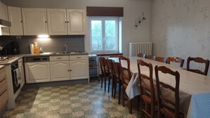 A kitchen with white cabinets, a stove, and a sink. There is a dining table with chairs and a window with a view of trees.