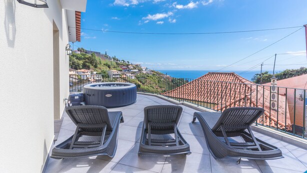 Ein Balkon mit drei Korlounge-Stühlen, einer Whirlwanne und freiem Blick auf das Meer und die Hügelstadt.