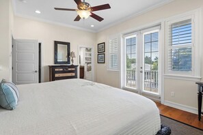 A bedroom with a bed, a ceiling fan, a dresser, a mirror, and a door leading to a balcony.