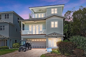 A two-story residential building with a garage, a balcony, and a lawn.