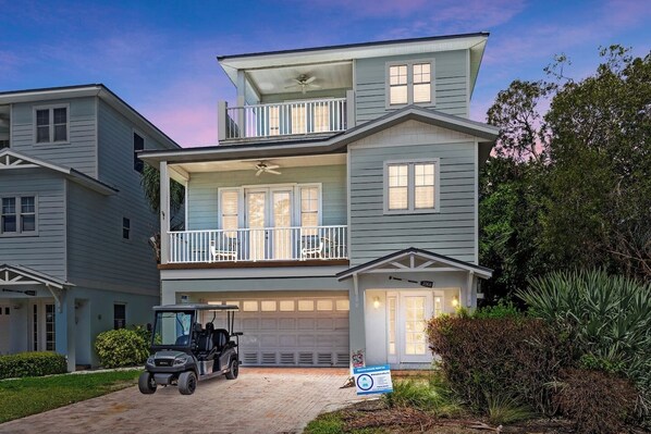 A two-story residential building with a garage, a balcony, and a lawn.