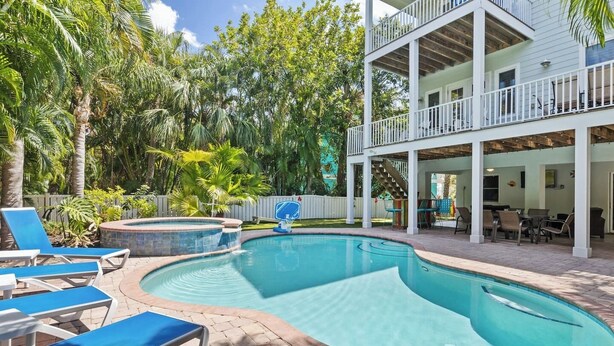 Una piscina con sillas de descanso, un jacuzzi y un patio cubierto con mobiliario exterior.