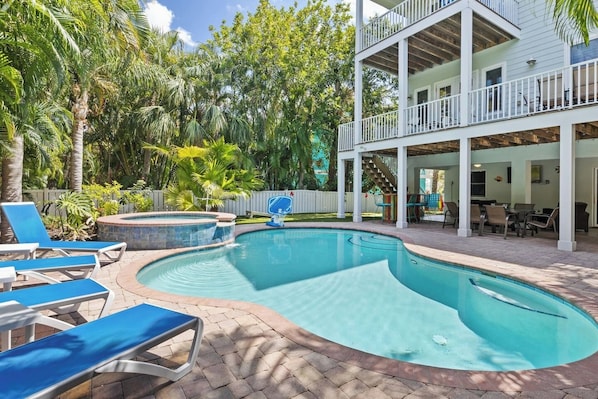 Une piscine avec des chaises longues, un jacuzzi et un patio couvert aménagé avec du mobilier d’extérieur.