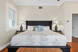 A bedroom with a large bed, two bedside tables with lamps, a window with blinds, and a door. - 2-Min walk to beach, Pool, Hot Tub, Putting Green! (Holmes Beach)