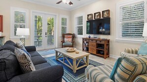 Una sala de estar con sofá, sillón, mesa de centro, televisor y objetos decorativos.