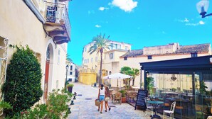 A narrow street with buildings on either side, outdoor seating, and a palm tree. - Sublime atypical apartment with terrace in the heart of ERBALUNGA (Brando)