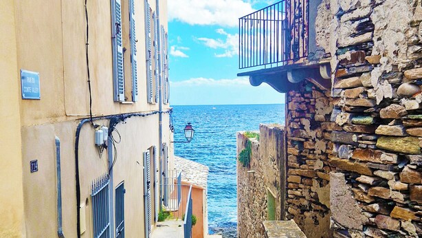 A narrow stone-paved street flanked by buildings with balconies overlooking a body of water. - Sublime atypical apartment with terrace in the heart of ERBALUNGA (Brando)