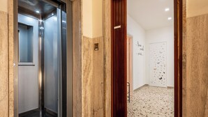 Een lift met een metalen afwerking, een houten deur en een betegelde vloer met een puntpatroon.