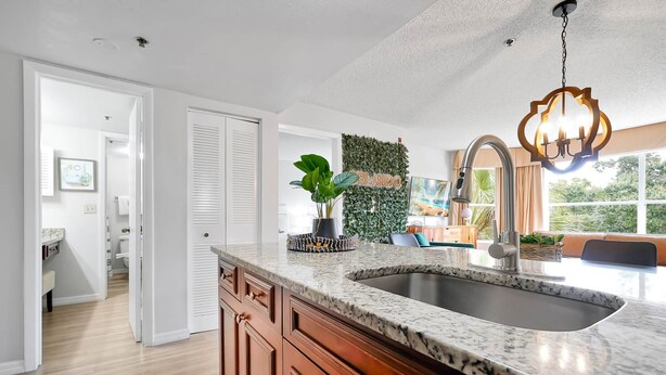 A modern kitchen with a granite countertop, stainless steel sink, and a hanging light fixture. - Parkside on I-Drive - Stay near ALL theme parks (Kissimmee)