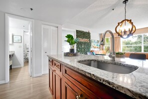 Uma cozinha moderna com bancada de granito, pia de aço inoxidável e luminária pendente.