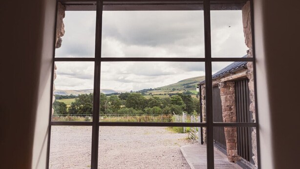 A view through a window with a stone building and a grassy field.