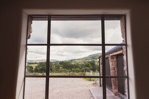 A view through a window with a stone building and a grassy field. - Swallow Barn at Greenclose Farm (Penruddock)