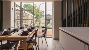 A dining area with a table set for four, a stone wall, and a view of a garden and buildings outside.