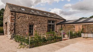 A stone building with a sloped roof, a fenced garden, and a metal gate.