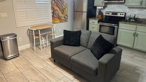 Una cocina compacta con un sofá gris, una pequeña mesa de comedor y un cubo de basura.