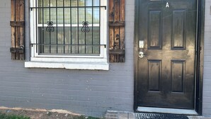 Una casa con puerta negra, ventana con barrotes y un pequeño porche.