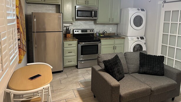 Cocina compacta con refrigerador, microondas, estufa y lavadora. Incluye un pequeño comedor con mesa y sofá.