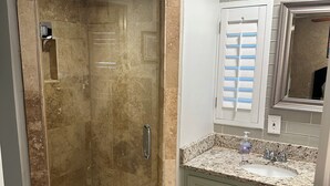 Un baño con ducha de vidrio, un lavamanos con encimera de granito y un mueble de tocador verde.