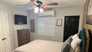 Un dormitorio con cama, cómoda, ventilador de techo, equipo de aire acondicionado y una puerta.