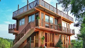 A multi-story building with a balcony on the upper level, a staircase leading to the entrance, and a small garden area. - 2 Room Loft w/ patio, parking, kitchen (Mazunte)
