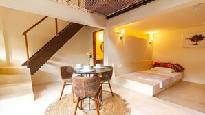 A compact room with a bed, a dining table with chairs, a staircase, and a wall-mounted lamp. - 2 Room Loft w/ patio, parking, kitchen (Mazunte)