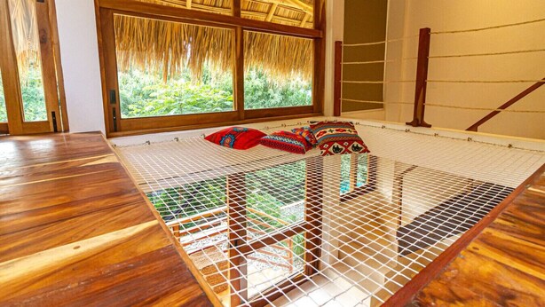 Une chambre avec un plancher en bois, un lit doté d’une moustiquaire et une fenêtre donnant sur un paysage verdoyant.