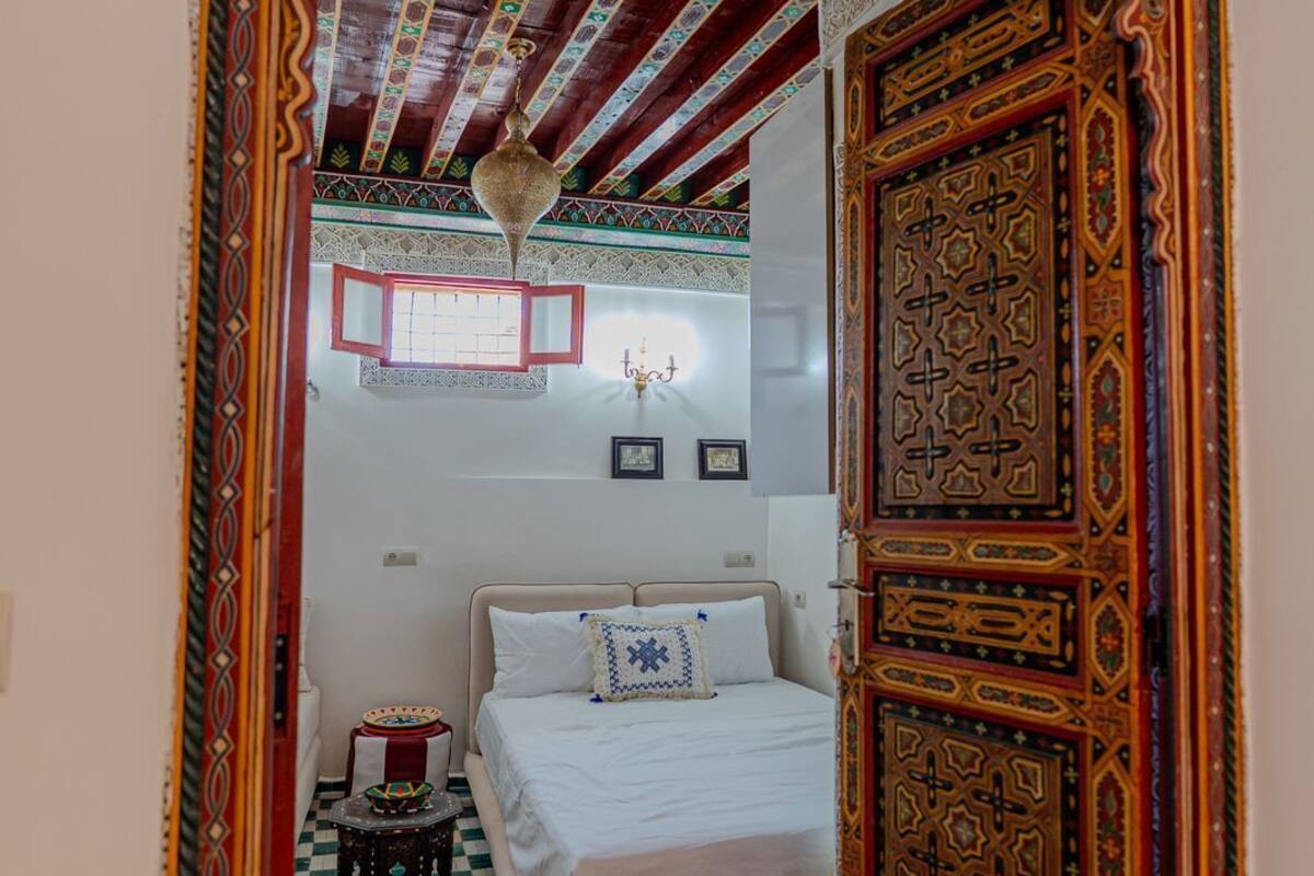Una habitación con una cama, una mesita, un tapete y una puerta decorativa.