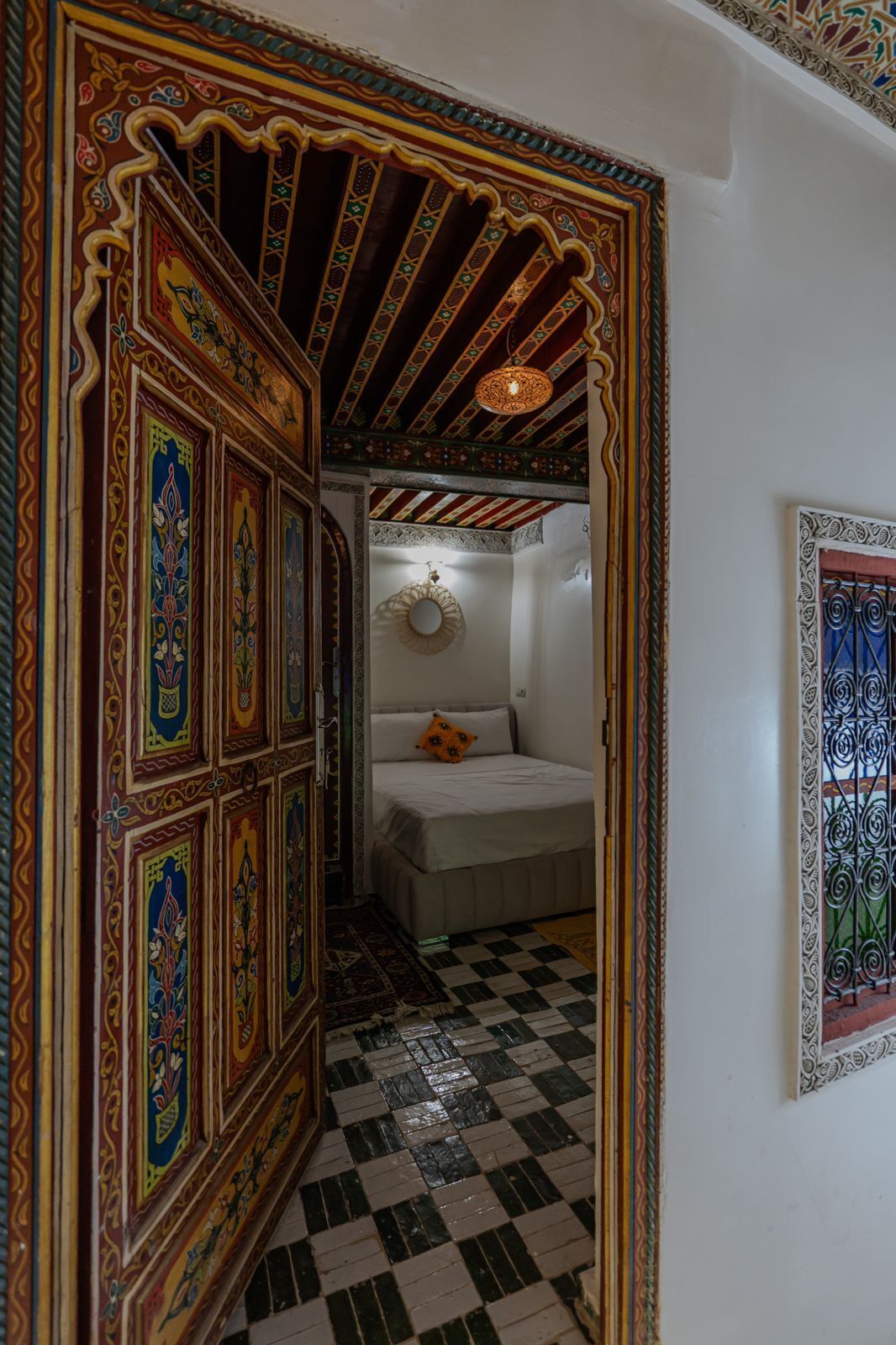 A room with a checkered floor, a bed with a pillow, and ornate wall decorations.