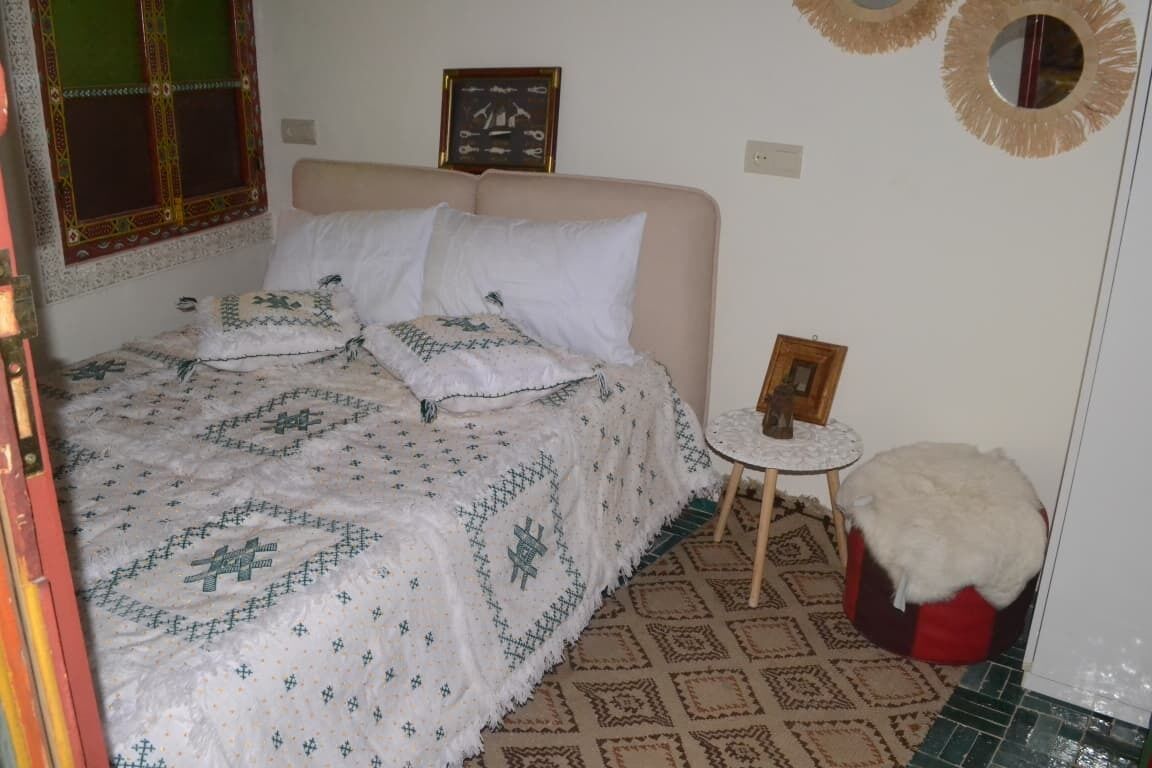 A bedroom with a bed, pillows, a small round table, and a chair.