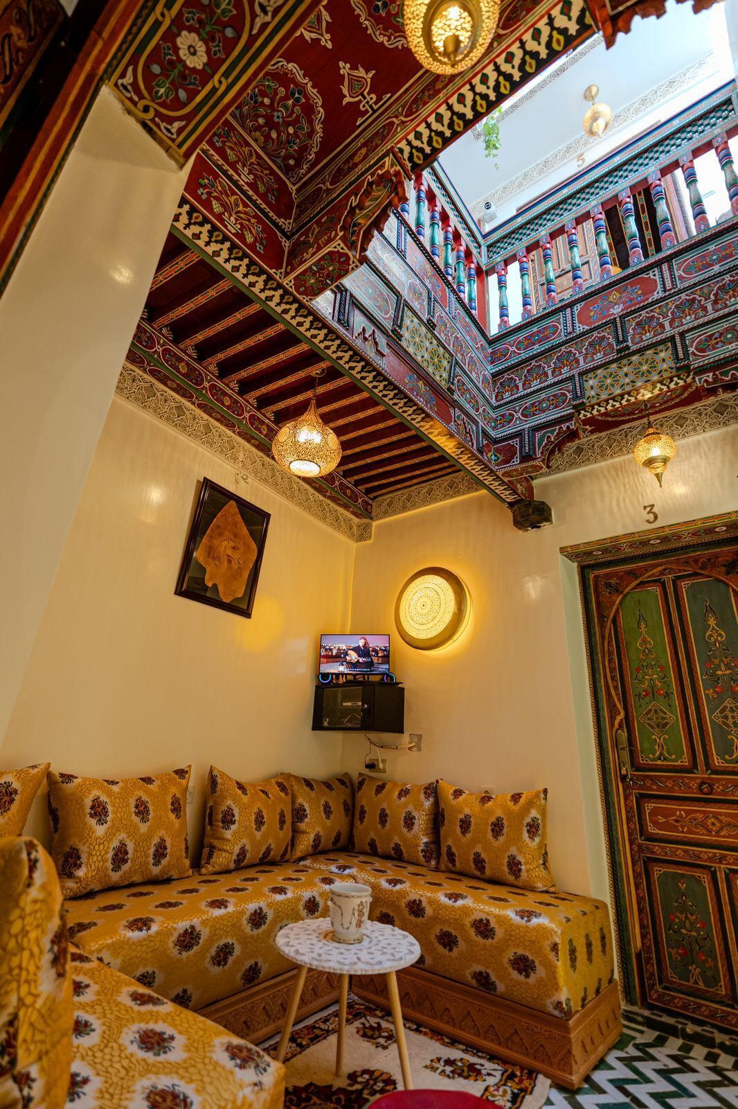 A traditional room with a sofa, a television, a decorative ceiling, and a patterned floor.