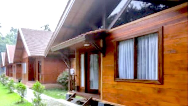 A row of wooden cabins with pitched roofs, small front yards, and a clear sky. - PAVO RESORT (Citaringgul)