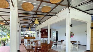 A spacious indoor area with high ceilings, exposed beams, and woven ceiling panels. There are several wooden tables and chairs arranged for dining or seating. - PAVO RESORT (Citaringgul)