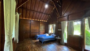 A wooden cabin room with two beds, a small table, and a window with curtains. - PAVO RESORT (Citaringgul)