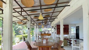 A covered outdoor dining area with a round wooden table and chairs, surrounded by a metal roof with woven ceiling panels. - PAVO RESORT (Citaringgul)