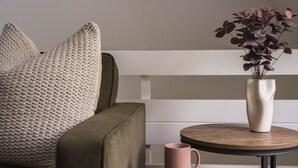 Et hyggeligt opholdsområde med en polstret sofa, et rundt træbord og en vase med lilla blomster.