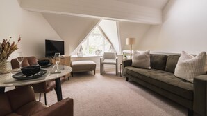 A modern loft bedroom with a sloped ceiling, a large window, a sofa, a dining table, and a TV. - A cosy, base for two in Windermere, perfect for laid-back Lake District getaways. (Windermere)