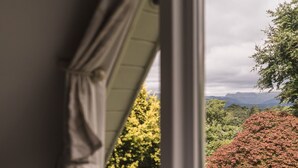 A view through a window with curtains, revealing a landscape with trees and mountains in the distance. - A cosy, base for two in Windermere, perfect for laid-back Lake District getaways. (Windermere)