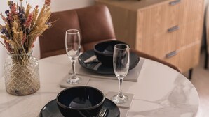 A dining table with a vase of dried flowers, two wine glasses, and black bowls on white plates. - A cosy, base for two in Windermere, perfect for laid-back Lake District getaways. (Windermere)
