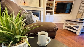 A cozy living room with a fireplace, a coffee table with a mug, and a potted plant. - Charming Country Getaway in Reilly Springs (Sulphur Springs)
